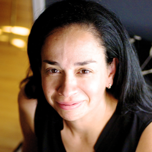 Head shot of Bern Irizarry, a middle-aged Latina with long dark hair, wearing a black blouse and smiling.