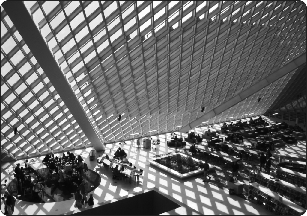Image of the exterior of Seattle Public Library’s Central Library; a daytime side view of the library depicting a modern steel and glass building on a tree-lined thoroughfare.