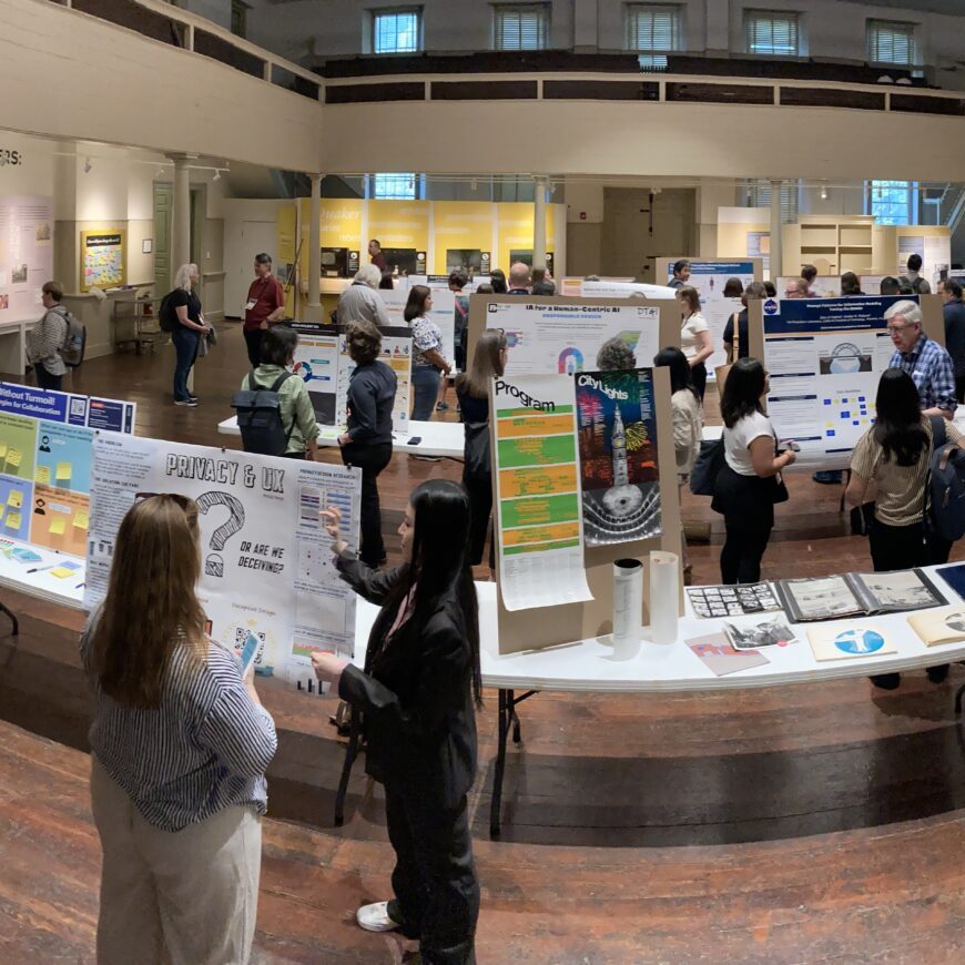 Wide-angled shot of a busy room at poster night. Many people talking around various posters.