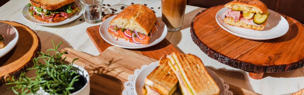 Table full of deli sandwiches, salad, and iced coffee